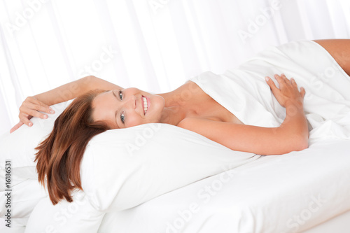 Smiling brown hair woman lying in white bed