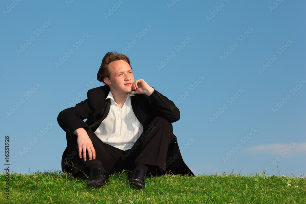 young man sits on meadow against sky young man sits on meadow against sky