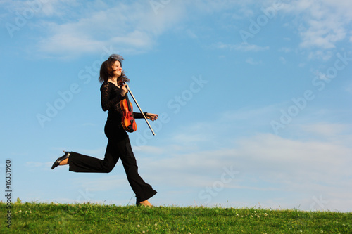 girl with violin runs on grass against sky, side view