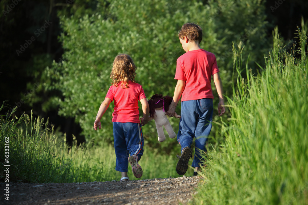 boy and girl go for a walk with doll in park, rear view