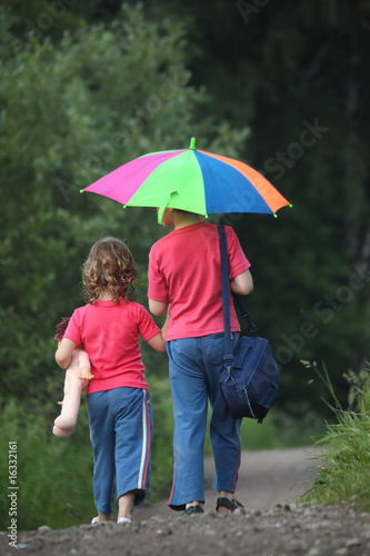 boy and girl go for a walk with umbrella in park, rear view
