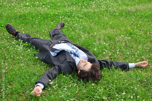 businessman lies on back on grass, having stretched legs and han
