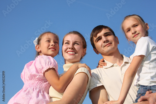 two parents hold children on hands against sky