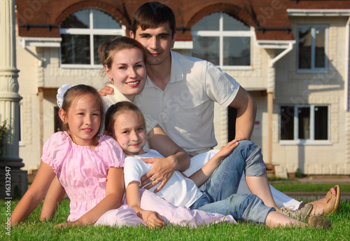 family from four sits on grass against house