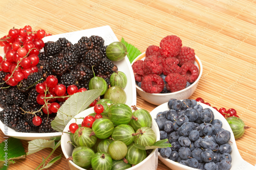 Berries in plates, on a table, among green leaves Berries in plates, on a table, among green leaves