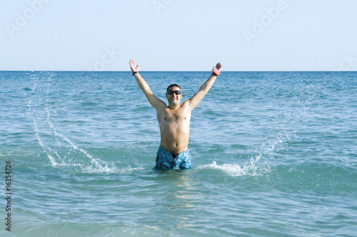 tanned man jumping out of the sea with splash