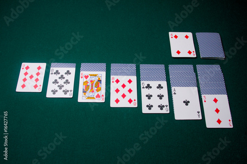 Playing cards are set up for a game of solitaire, on green felt photo