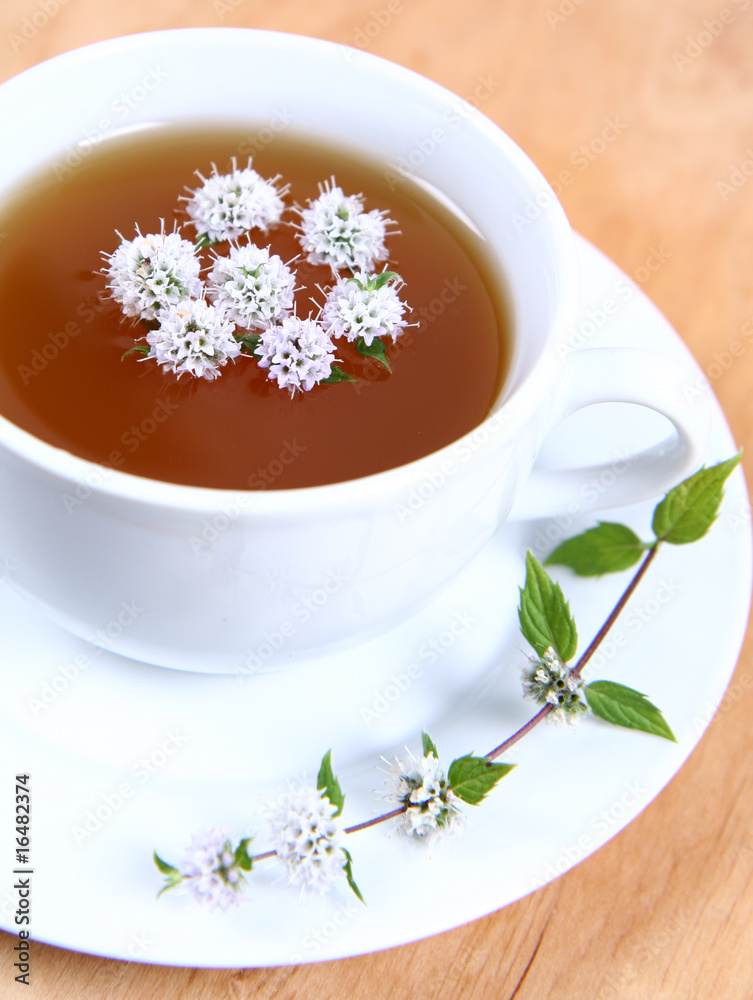 Cup of green tea with flowers of peppermint floating in it Cup of green tea with flowers of peppermint floating in it