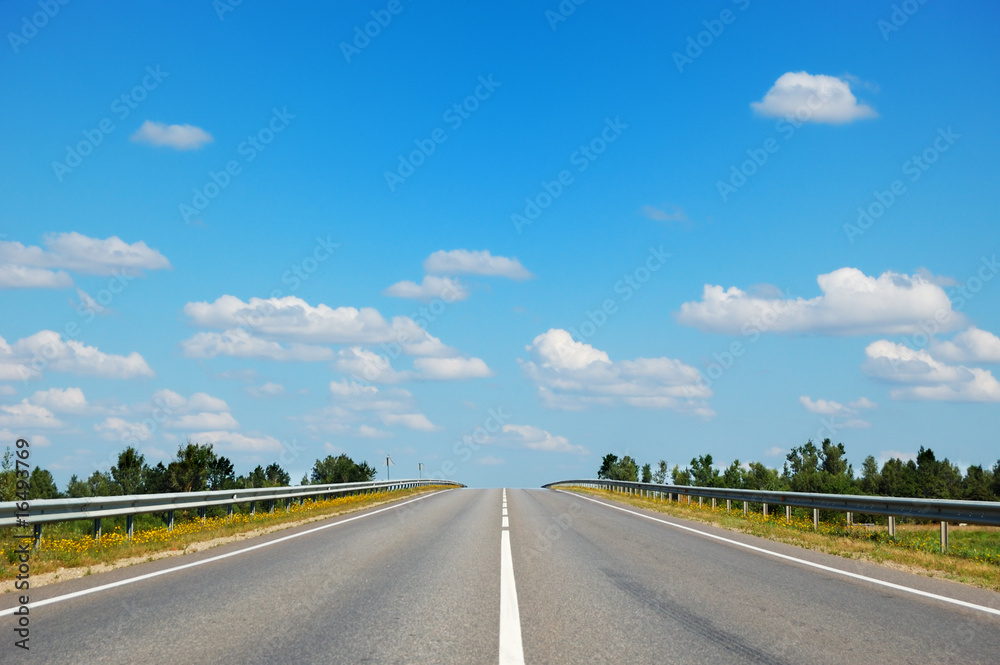 Fototapeta premium Empty countryside road leading straight to cloudy blue sky