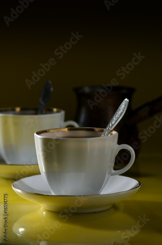 Two cups of coffee and coffee pot on a yellow-black background
