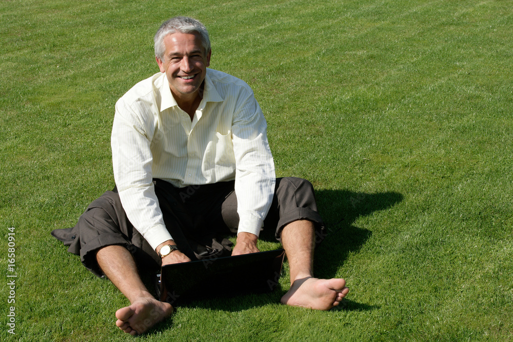 Barefoot businessman sitting on grass and using laptop Barefoot businessman sitting on grass and using laptop