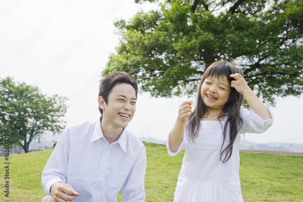 たんぽぽの綿毛を手に持つ女の子とそばで微笑む父親