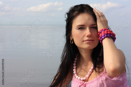 Dark-haired girl in pink sleeveless shirt against water and sky photo