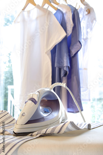 Fotografia, Obraz Iron on ironing board with clothes hanging
