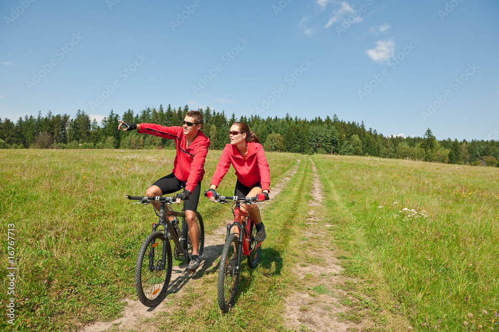 Sportive couple riding mountain bike in meadow Sportive couple riding mountain bike in meadow