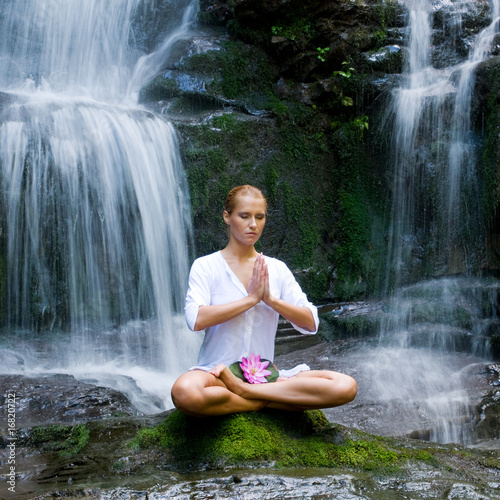 Young woman doing yoga near waterfalls