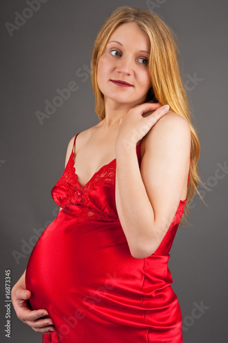 young pretty pregnant blonde in red dress isolated over gray