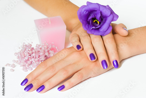 Hands with purple manicure and flower, pink candle and beads
