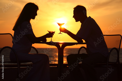 Female and man's silhouettes on sunset sit at table with two gla