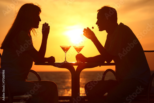 Female and man's silhouettes on sunset sit at table with glasses