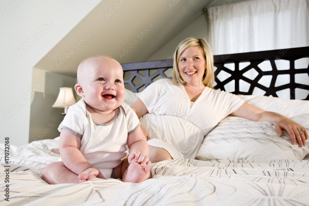 Happy 7 month old baby sitting on bed with mother Happy 7 month old baby sitting on bed with mother