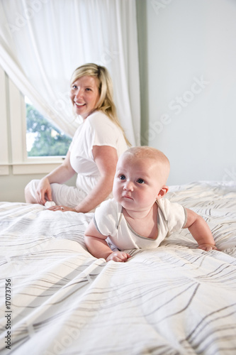 Cute baby crawling on bed while mother watches
