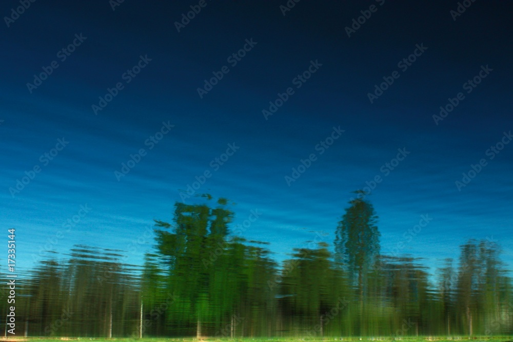 Reflections of green trees with light and dark blue sky.