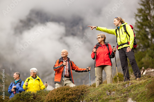 Fototapete Junger weiblicher wandernder Führer, der ältere Gruppe zeigt, die Berg umgibt