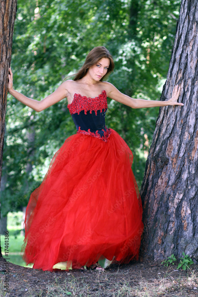 A beautiful woman in a red dress standing among trees in park
