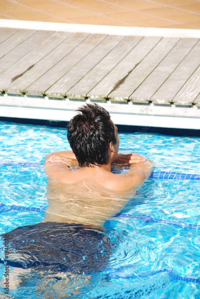 Young man relaxing at the edge of the swimming pool