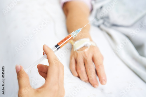 Hand holding injection with patient hand on background