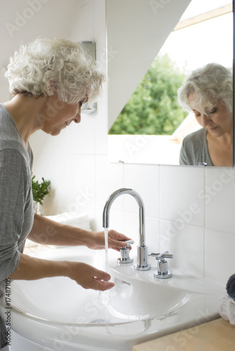 ältere Frau am hellen , weißen Waschbecken
