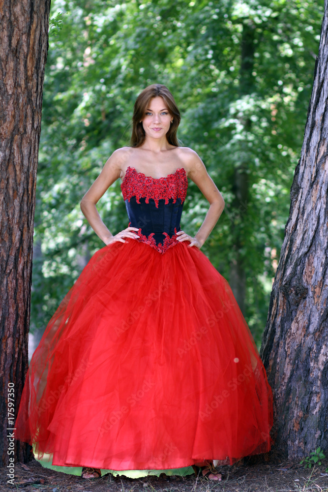 A beautiful woman in a red dress standing among trees in park A beautiful woman in a red dress standing among trees in park