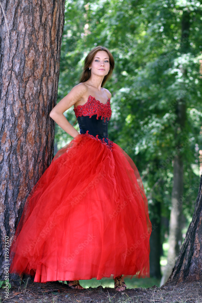 woman in a red dress standing among trees in park