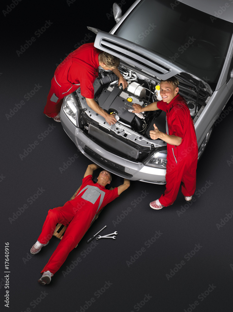 KFZ Mechaniker arbeiten an silbernem Auto KFZ Mechaniker arbeiten an silbernem Auto
