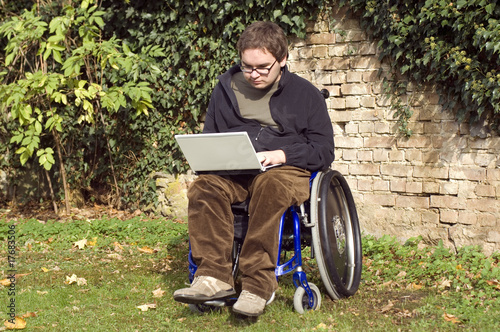 junger Rollstuhlfahrer. Student mit Laptop im Park photo