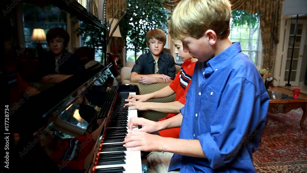 Two adolescent boys playing piano while a third looks on.