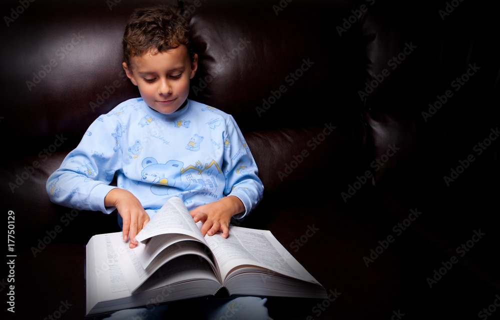 Cute kid reading a big book on a sofa Cute kid reading a big book on a sofa