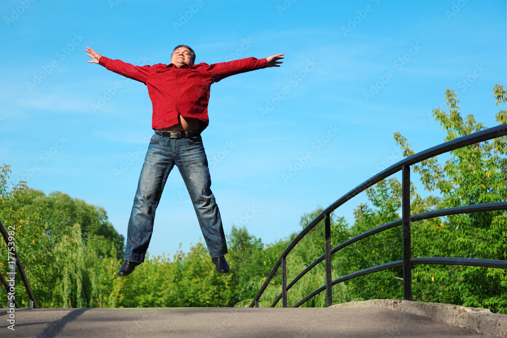 man in red shirt jumps outdoor in summer on bridge man in red shirt jumps outdoor in summer on bridge