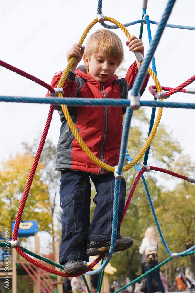 boy on playground climbing net of ropes boy on playground climbing net of ropes