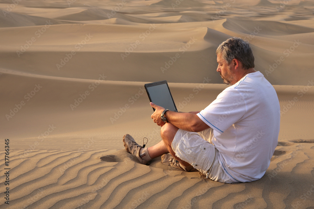 Man with laptop sitting in the desert.