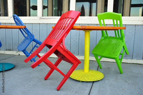 Red, Green, and Blue Chairs Leaning on Tables