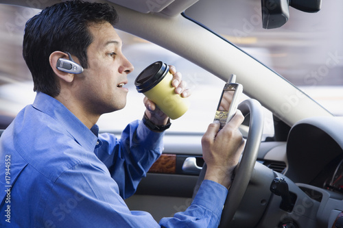 Hispanic businessman using cell phone drinking coffee and driving
