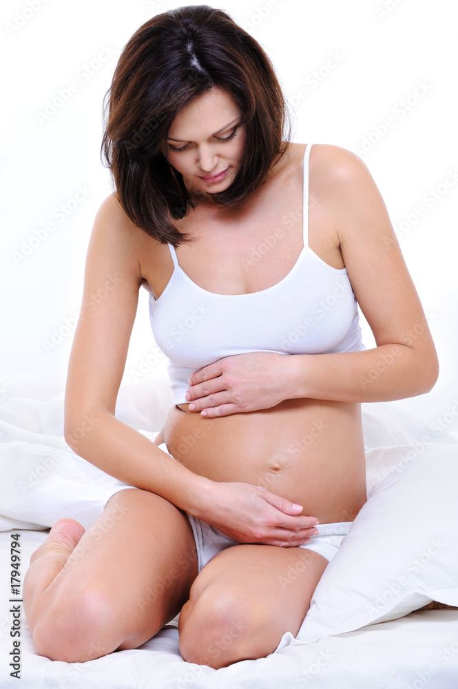 Pregnant woman sitting on bed and stroking her tummy Pregnant woman sitting on bed and stroking her tummy