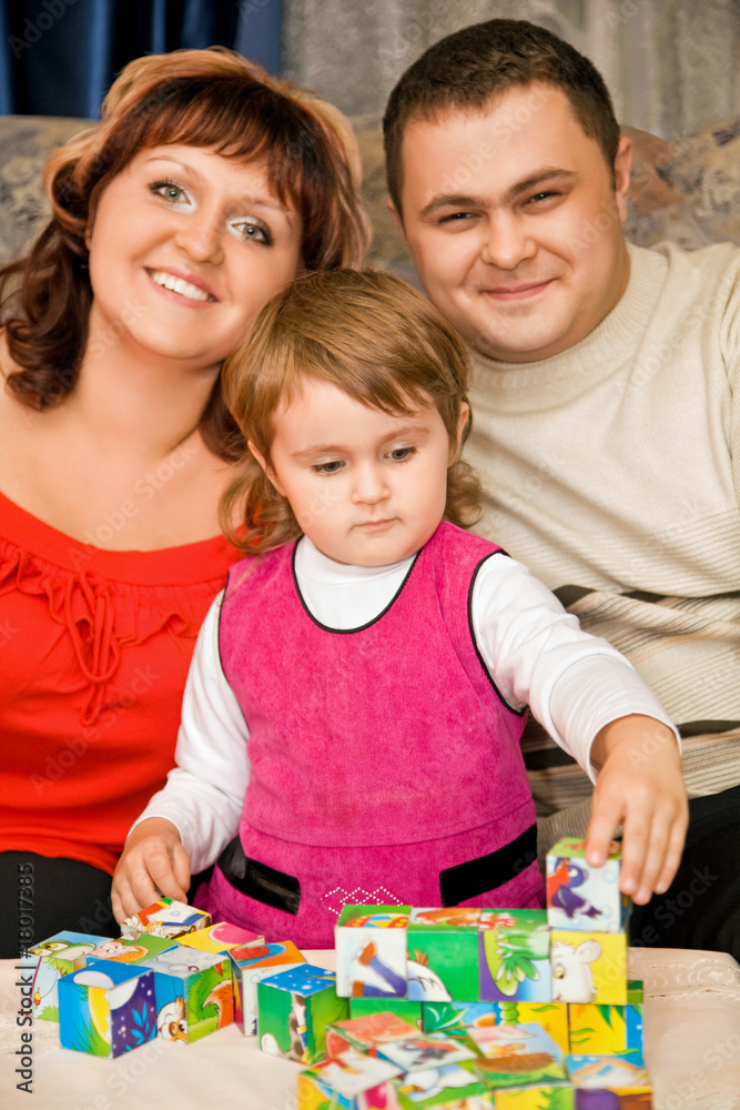 Fototapeta premium Married couple and little girl playing cubes in a cosy room