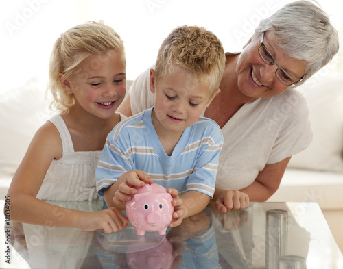 Foto Grandmother and children saving money in a piggybank