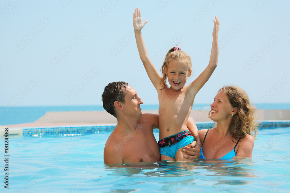 smiling parents play with daughter with hands up in water smiling parents play with daughter with hands up in water