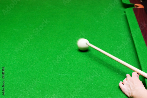 hand hitting with billiard cue a white ball in motion