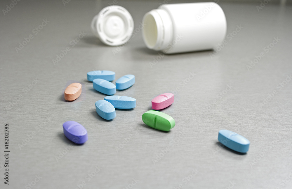 Colored pills spilling out of a white container (shallow DOF) Colored pills spilling out of a white container (shallow DOF)