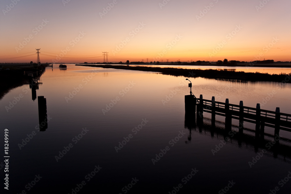 Beautiful sunrise above a dutch river while a ship is approachin